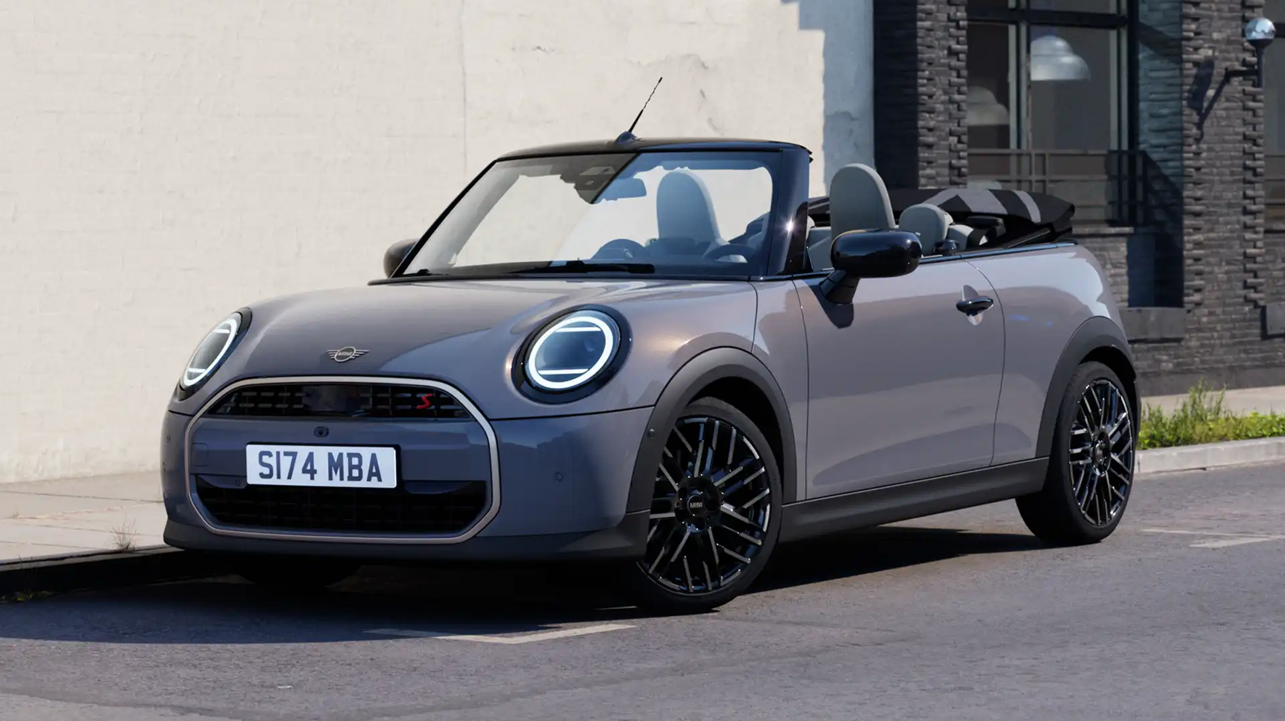 Mini Cabrio gris descapotable aparcado junto a un edificio moderno.