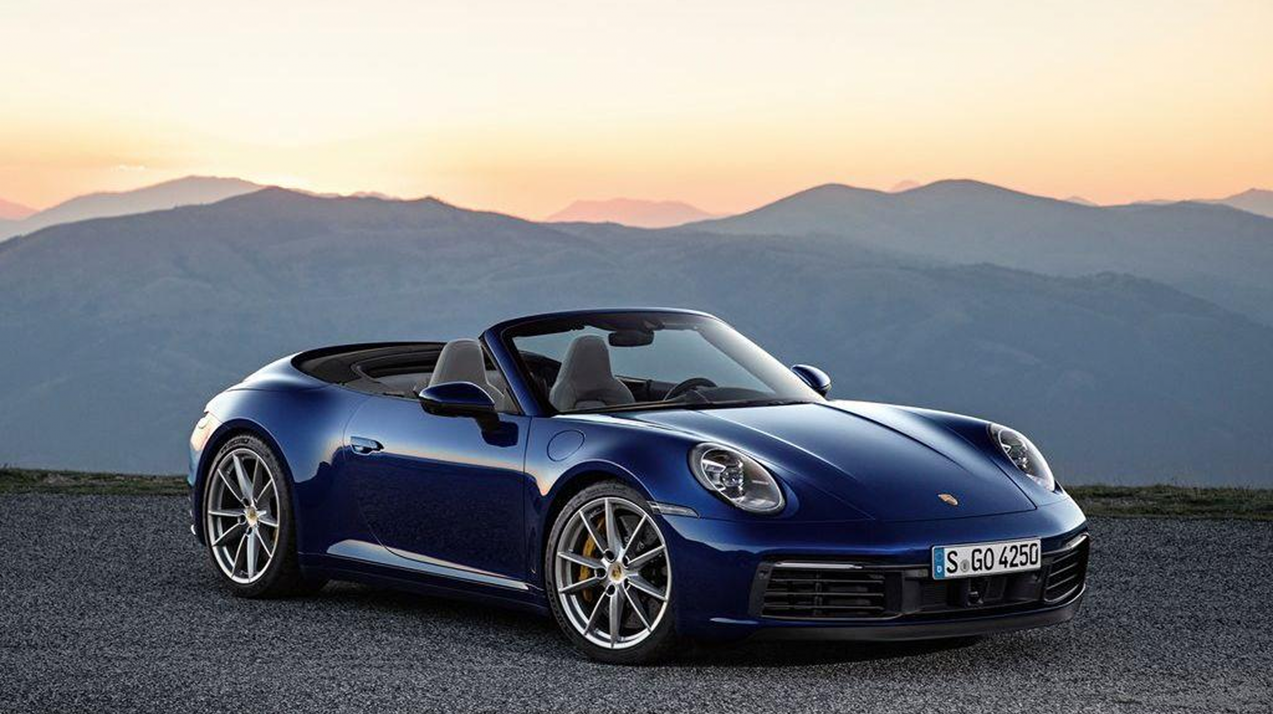 Porsche 911 Carrera 4S Cabriolet azul al atardecer, con techo descapotado.